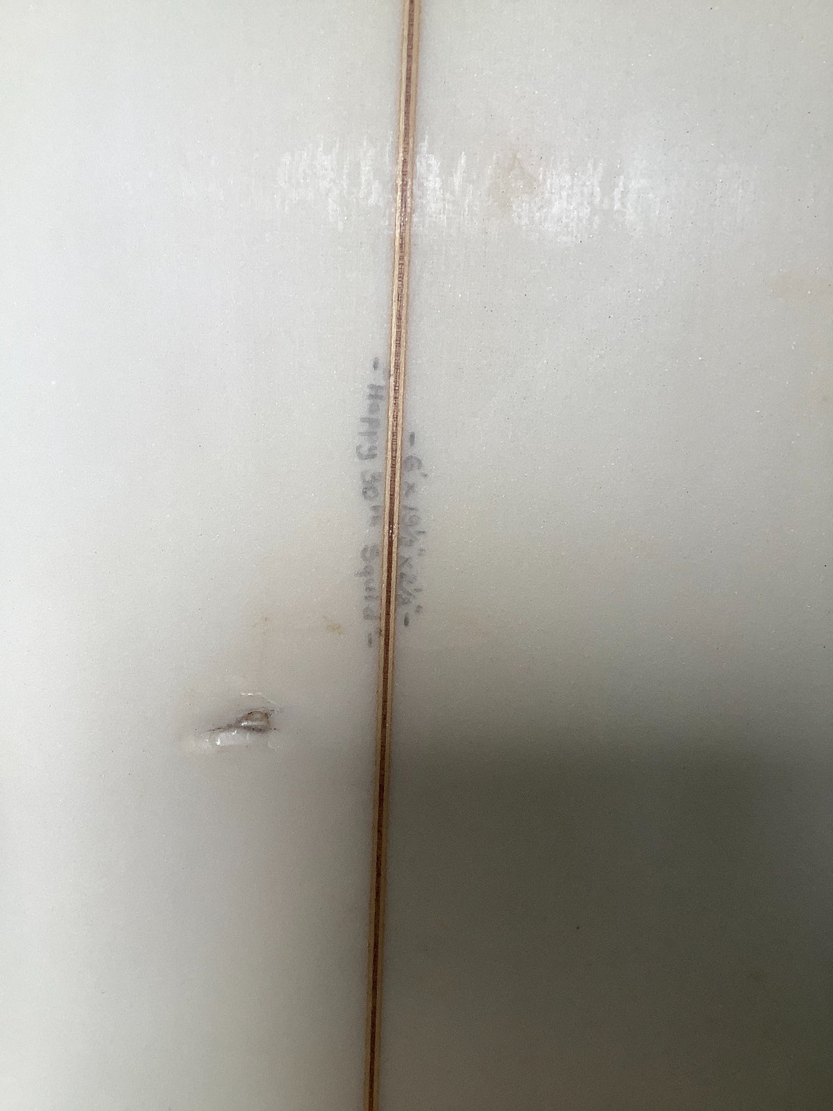 Close-up of handwritten surfboard dimensions and visible surface mark