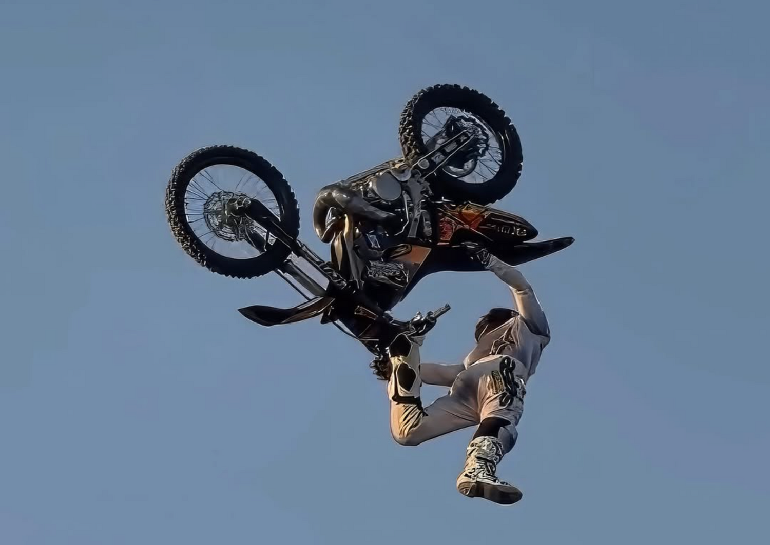 Person performing a motorcycle trick against a clear blue sky.