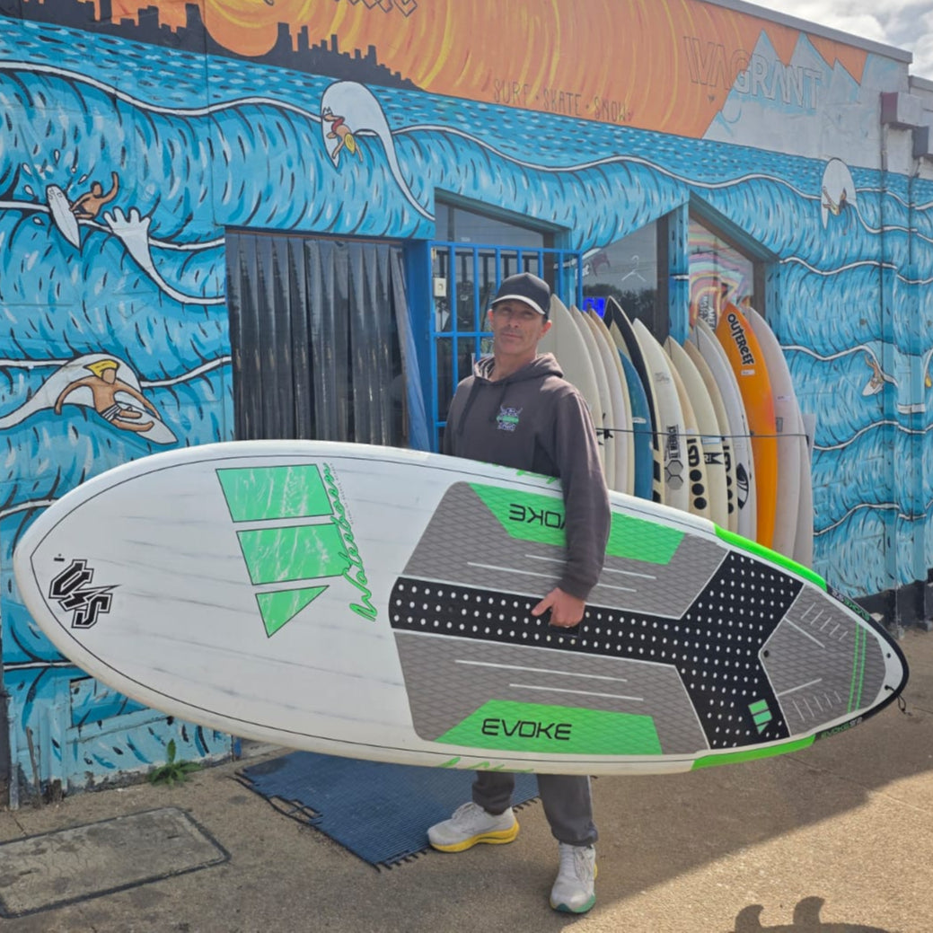 Person holding a surfboard in front of a colorful mural on a building.