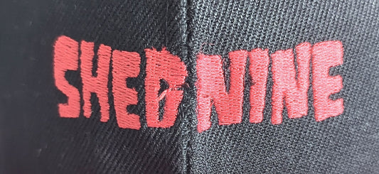 Gray cap with 'SHED NINE' embroidered in red on a dark background