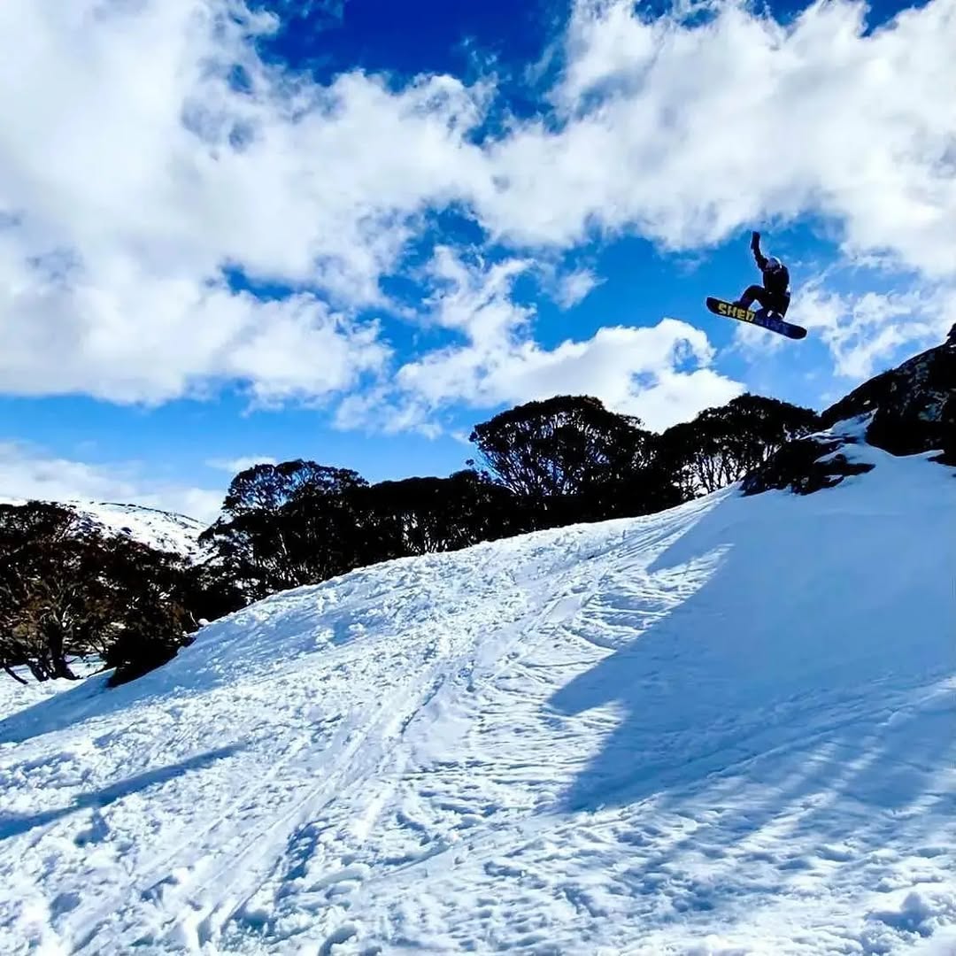 Person snowboarding in mid-air over a snowy slope with a blue sky and clouds.