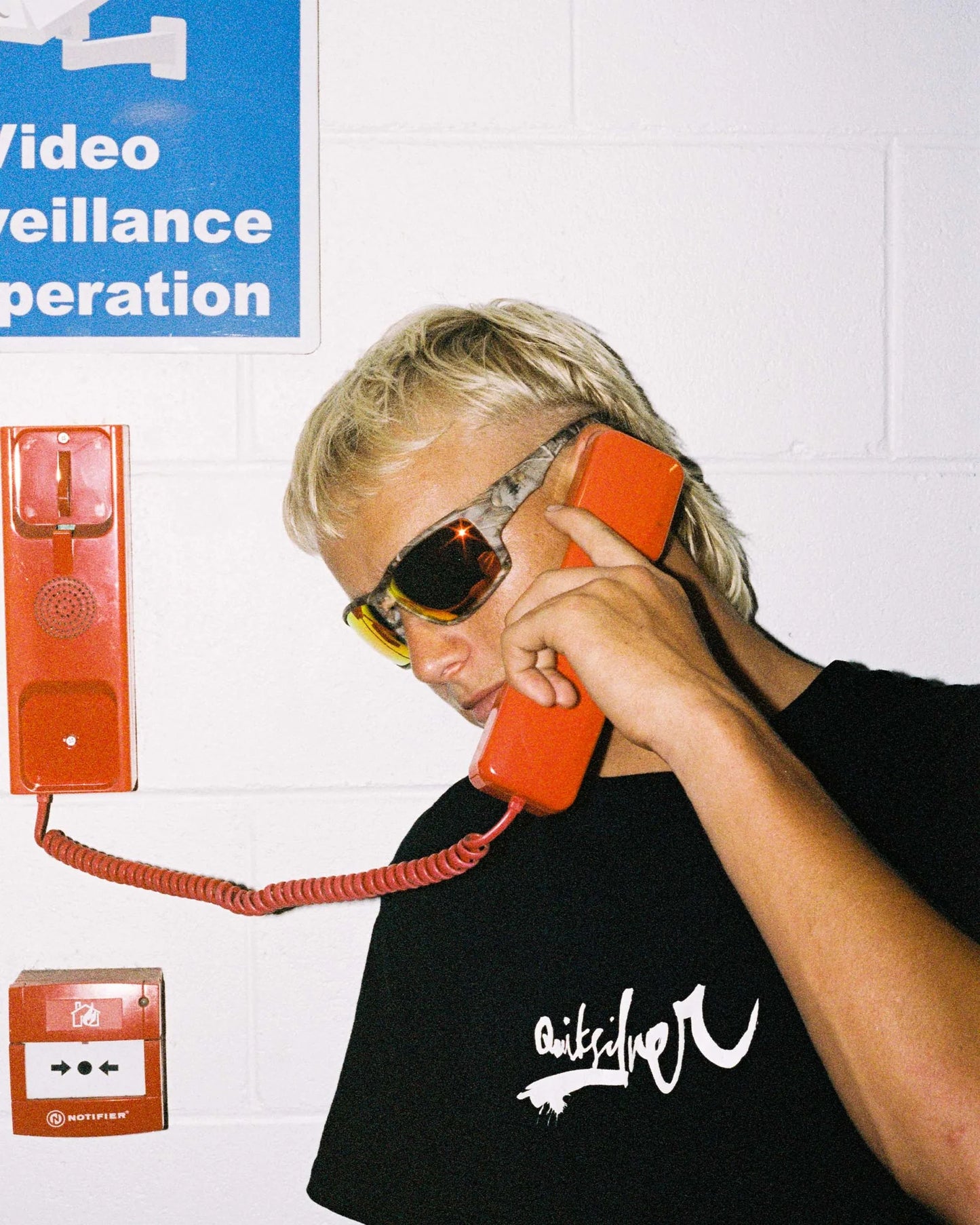 Portrait of model wearing Ritual Vision The Decline Sunglasses in Black / Black Polarised 63 mm while on the phone shed nine