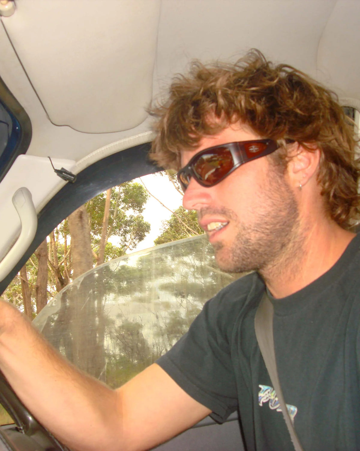Lifestyle image of model wearing Ritual Vision The Vacationer Sunglasses in Matte Black / Black Polarised while driving shed nine