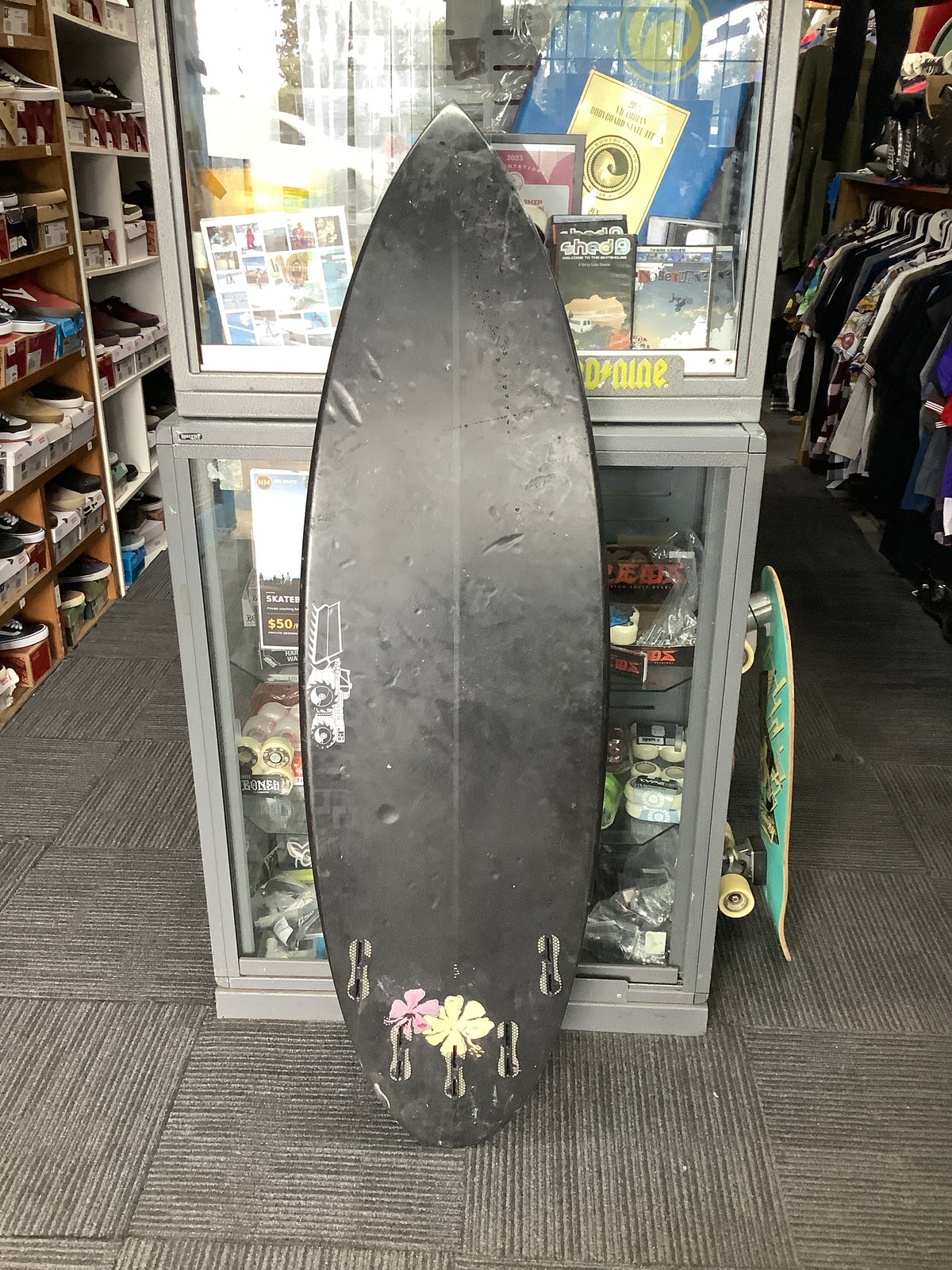 Second-hand black JS Industries surfboard underside with five fin boxes and flower stickers