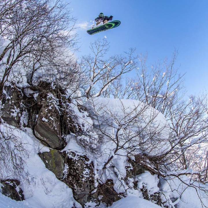 Person snowboarding off a cliff in a snowy landscape with clear blue sky