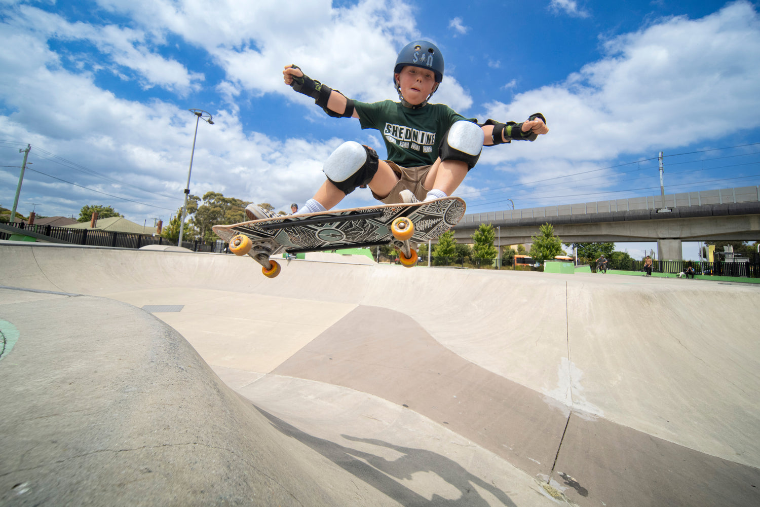 Child skateboarding at a skate park with a clear blue sky.