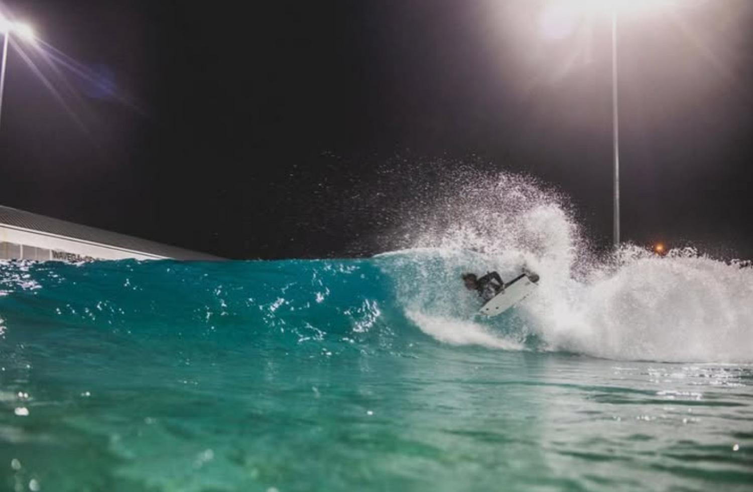 Person surfing a wave at night with artificial lights illuminating the scene.