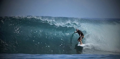 Surfer riding a wave in the ocean with a clear sky.