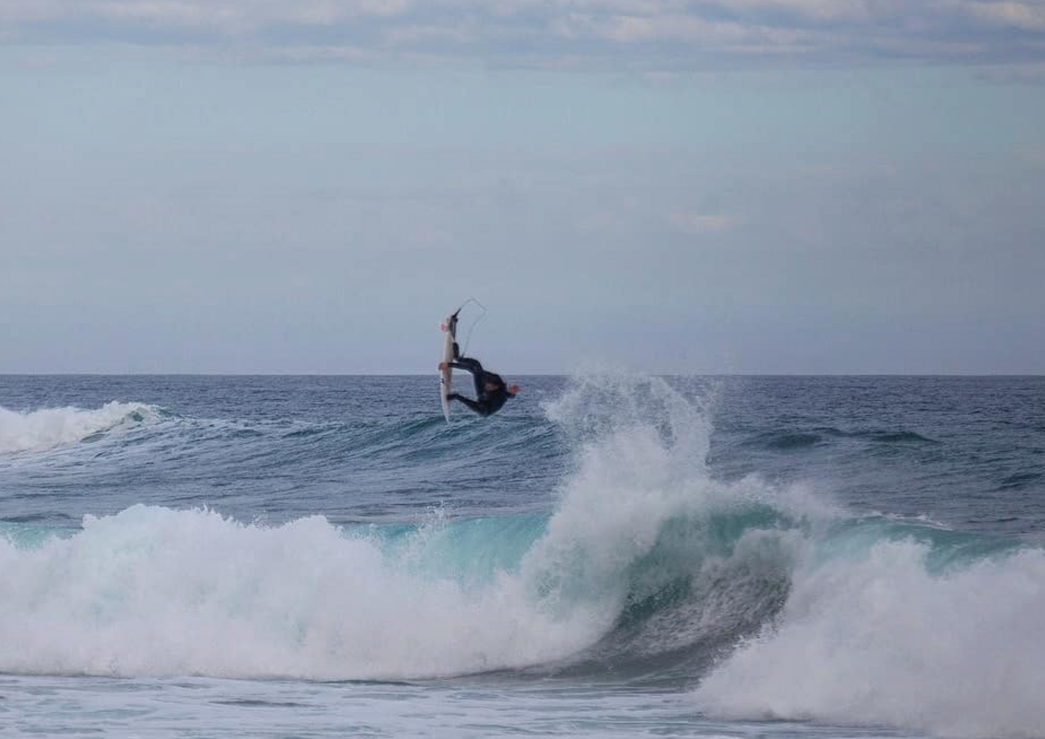 Person surfing a wave in the ocean with a clear sky.