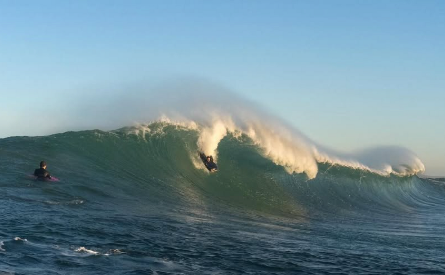 Surfer riding a wave in the ocean with clear blue sky
