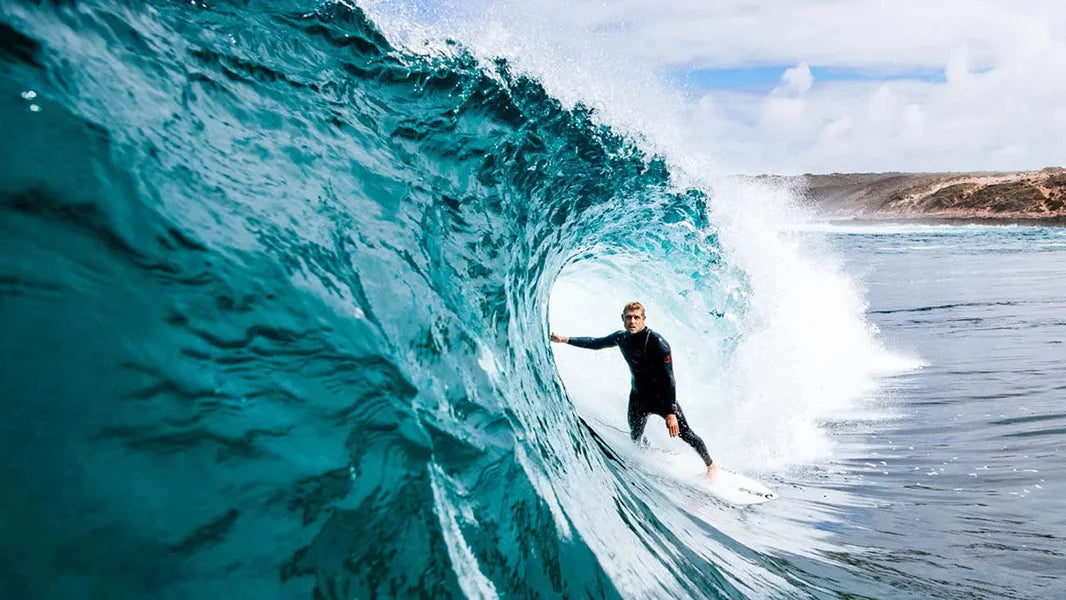 Person surfing a large wave with a clear sky in the background shed nine