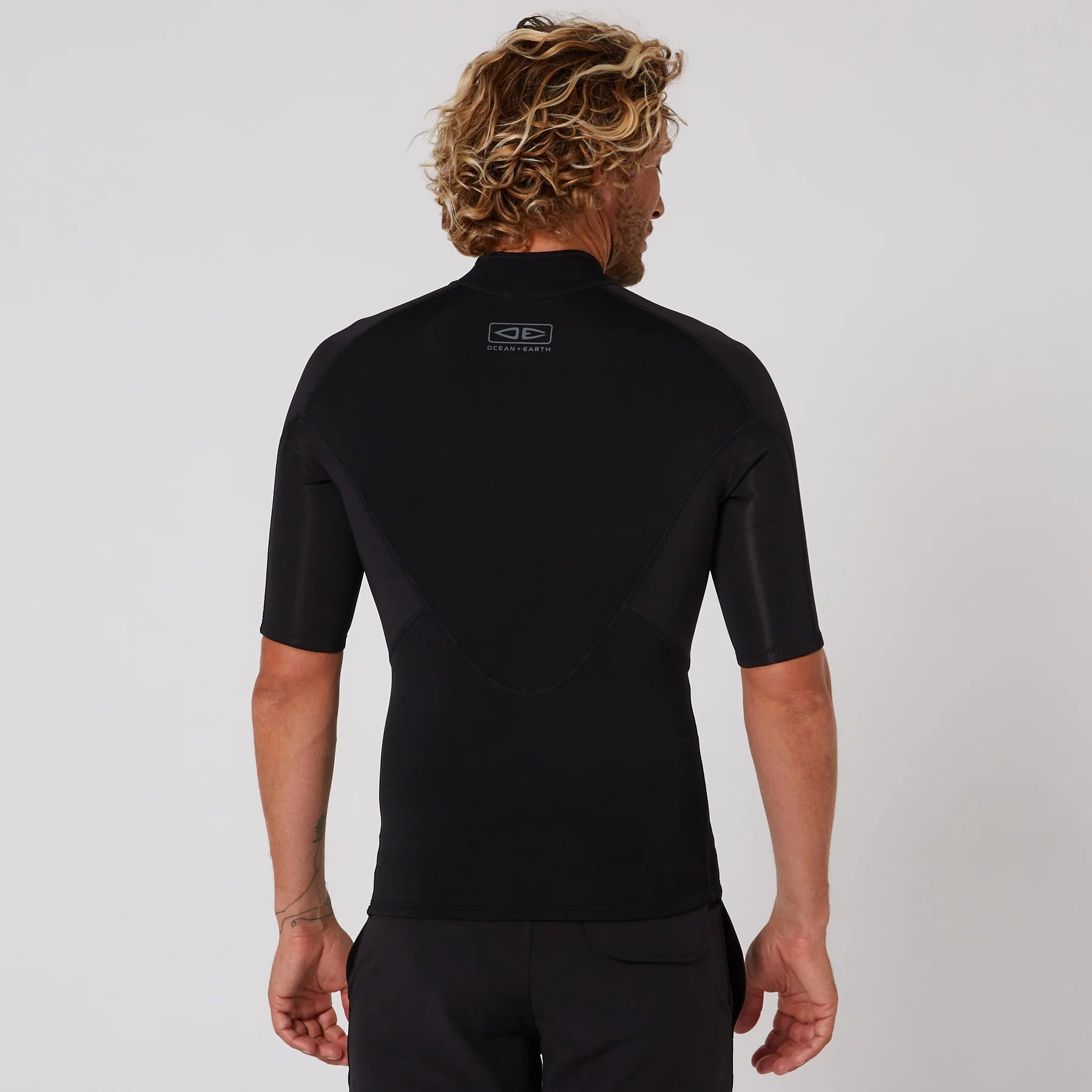 Person wearing a black short-sleeve shirt with a logo on the back against a light gray background shed nine