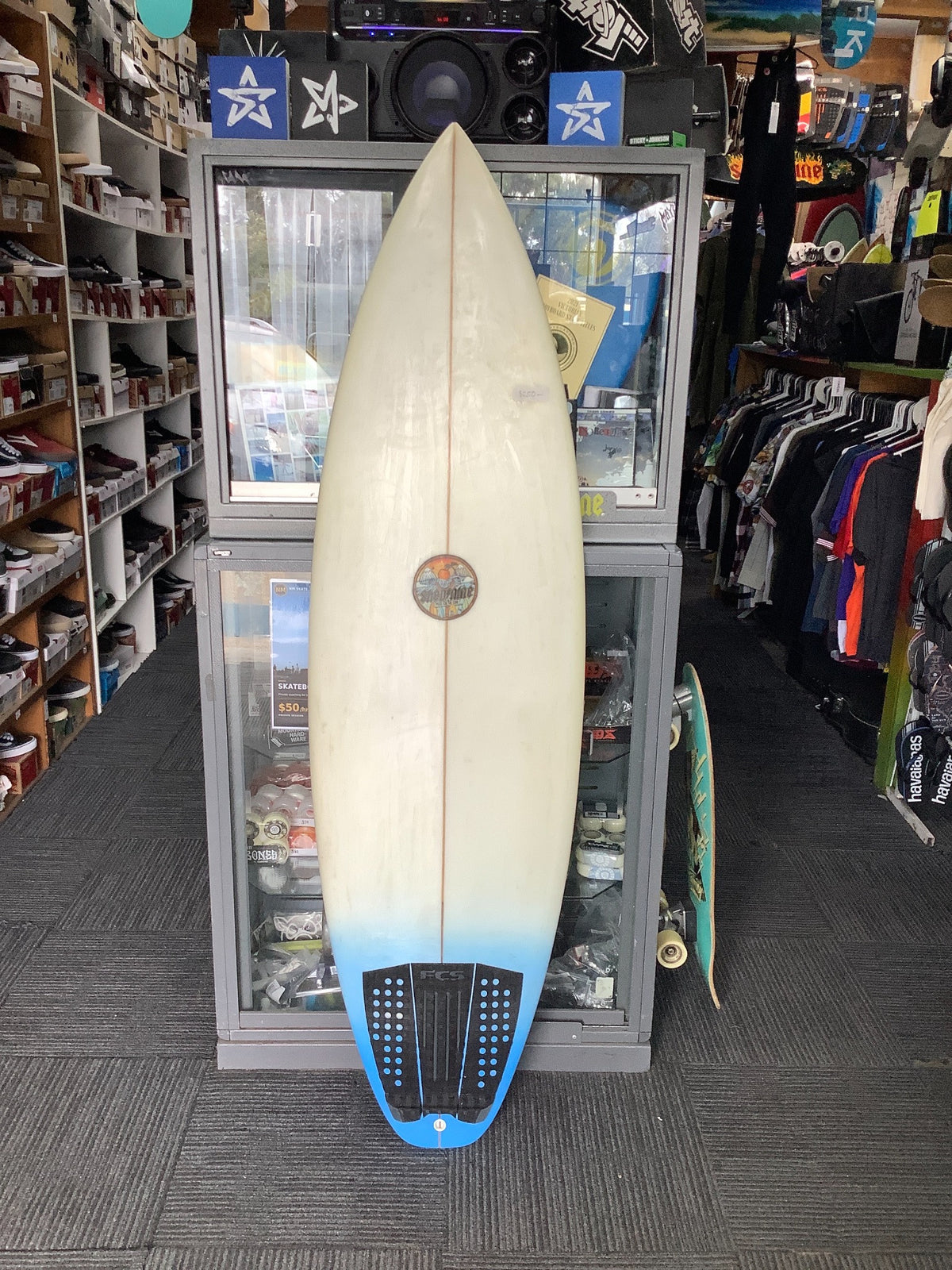 Deck view of used Shed 9 Custom 6'2 surfboard with cream finish, blue tail and black traction pad