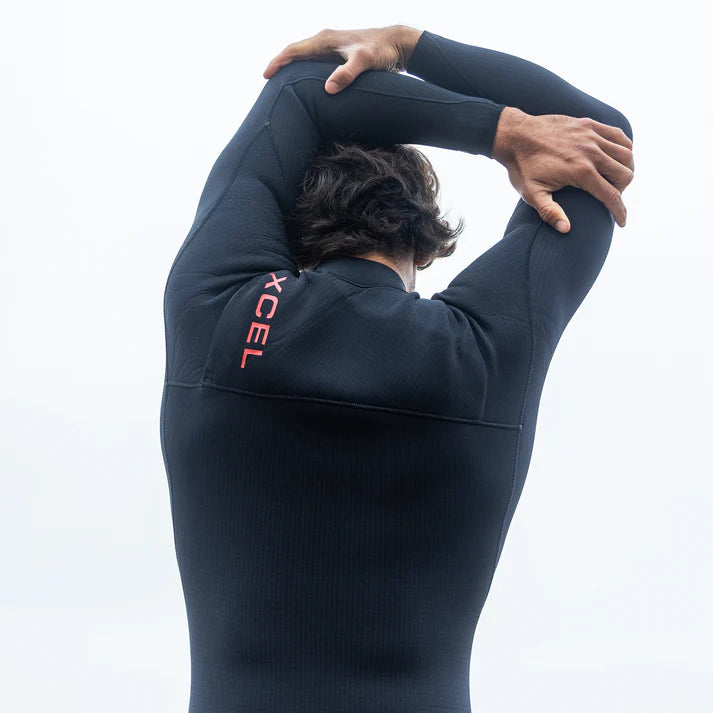 Person wearing a black wetsuit with 'XCEL' branding, stretching on a white background shed nine