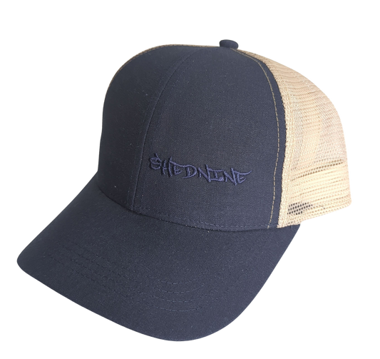 Navy blue and beige trucker cap with 'Shed Nine' logo on a white background