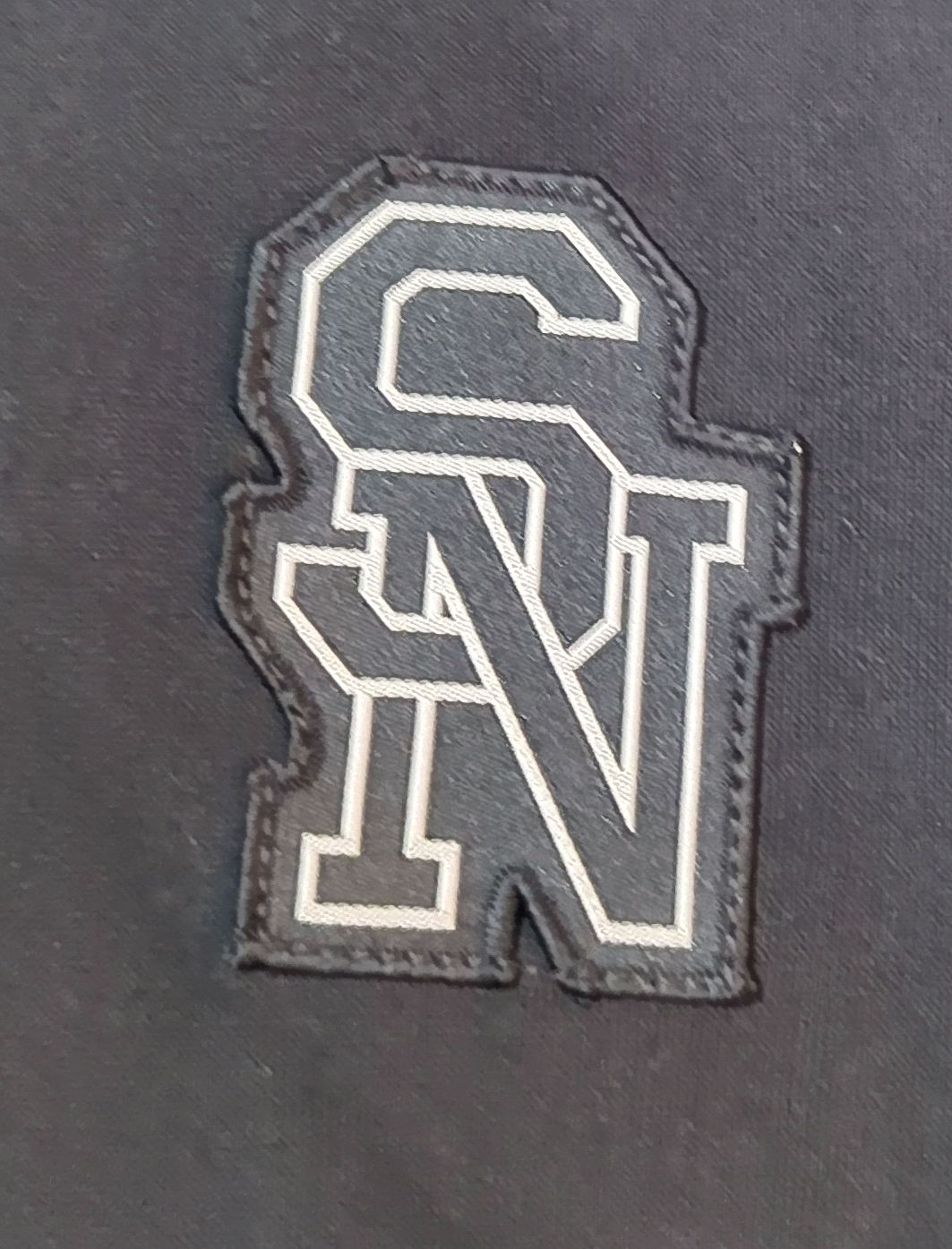 Embroidered patch with 'SN' initials on a dark fabric background