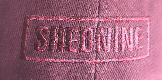 Close-up of a pink cap with 'SHEDNINE' embroidered on it.