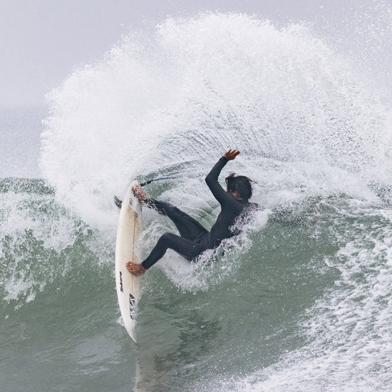 Surfer wearing Xcel Men’s Comp 3/2mm Chest Zip Steamer Wetsuit in black in the water