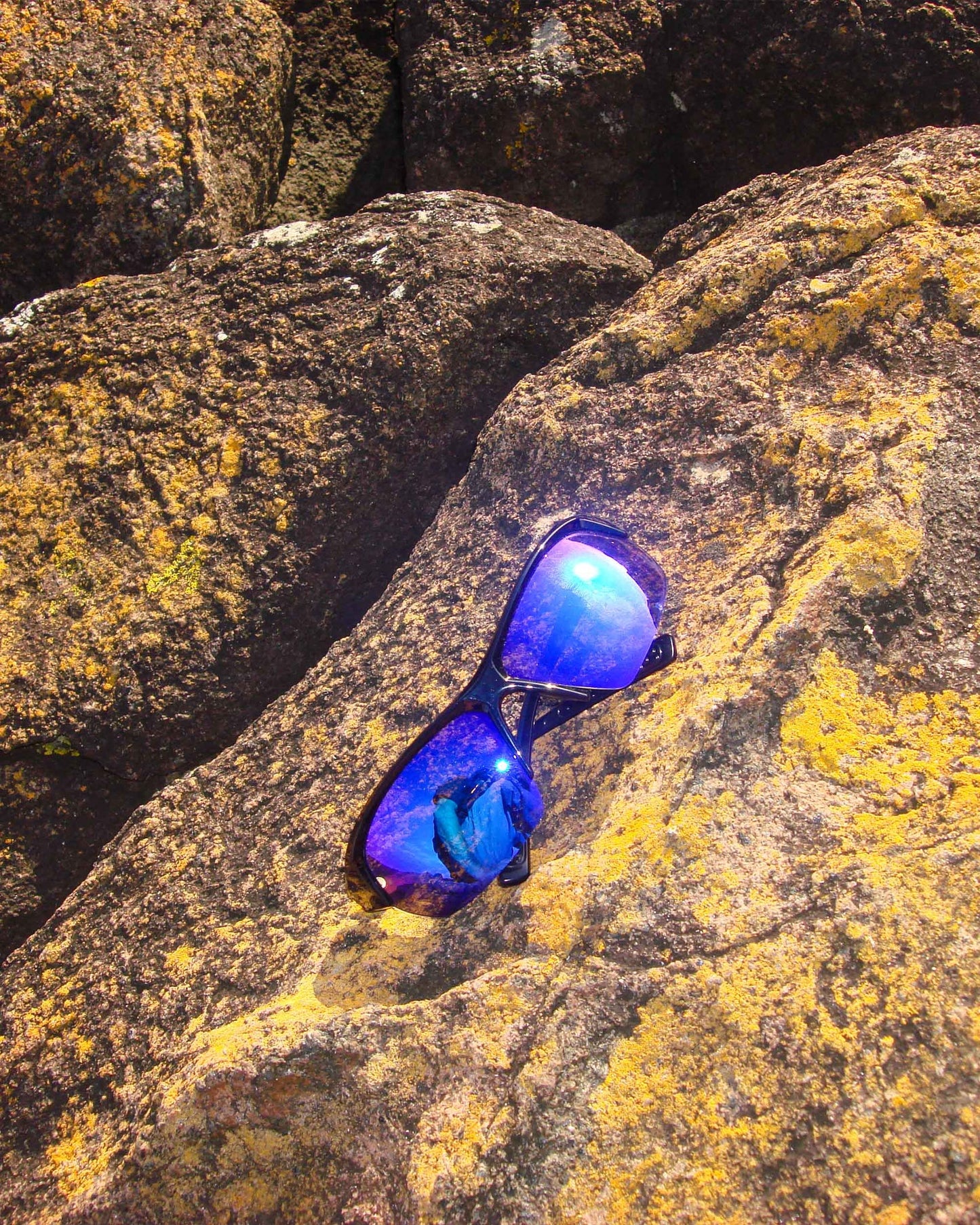 Product detail of Ritual Vision Break & Enter Sunglasses in Metallic Black / Bronze resting on rocks shed nine