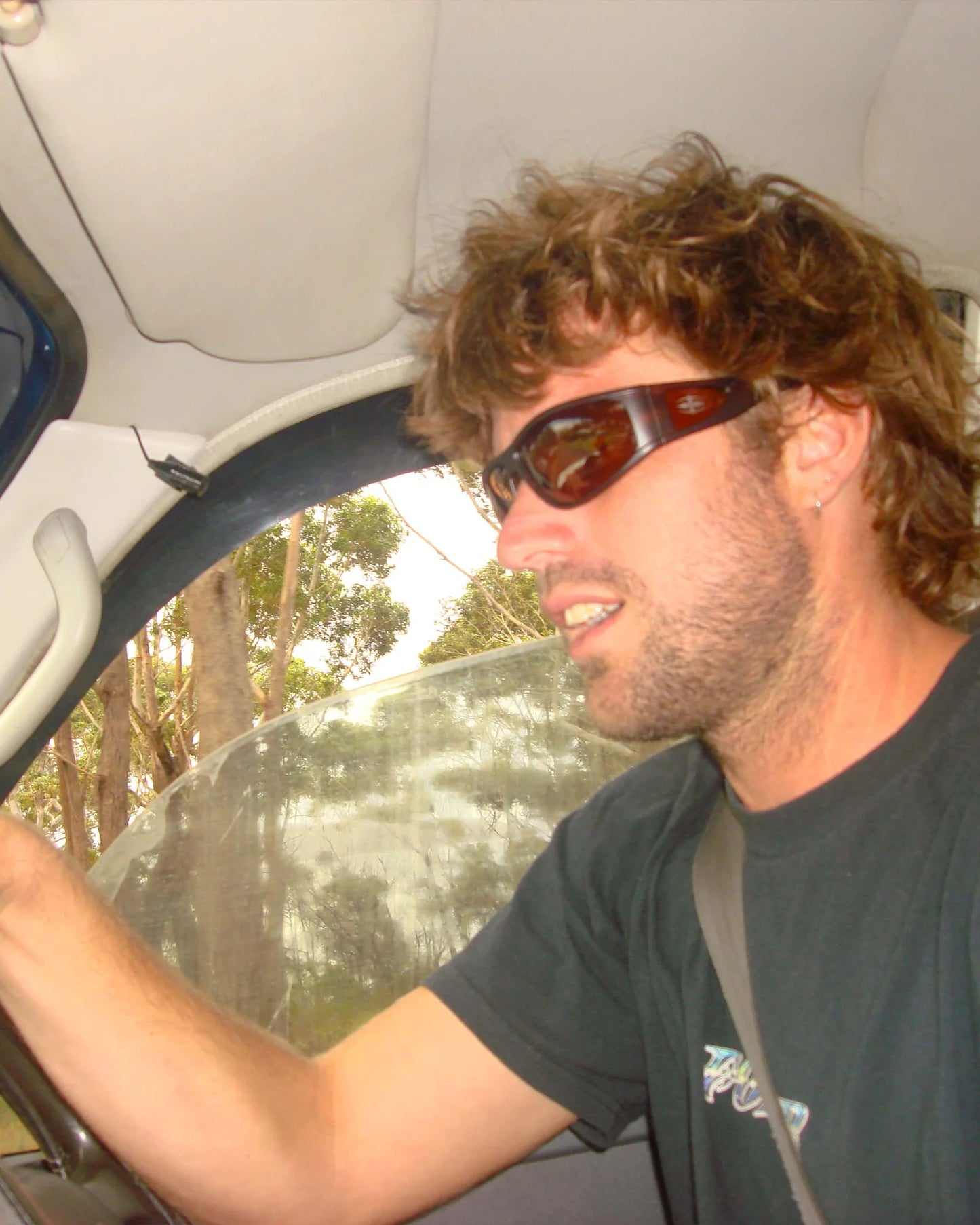 Lifestyle image of model wearing Ritual Vision The Vacationer Sunglasses in Matte Black / Black Polarised while driving shed nine