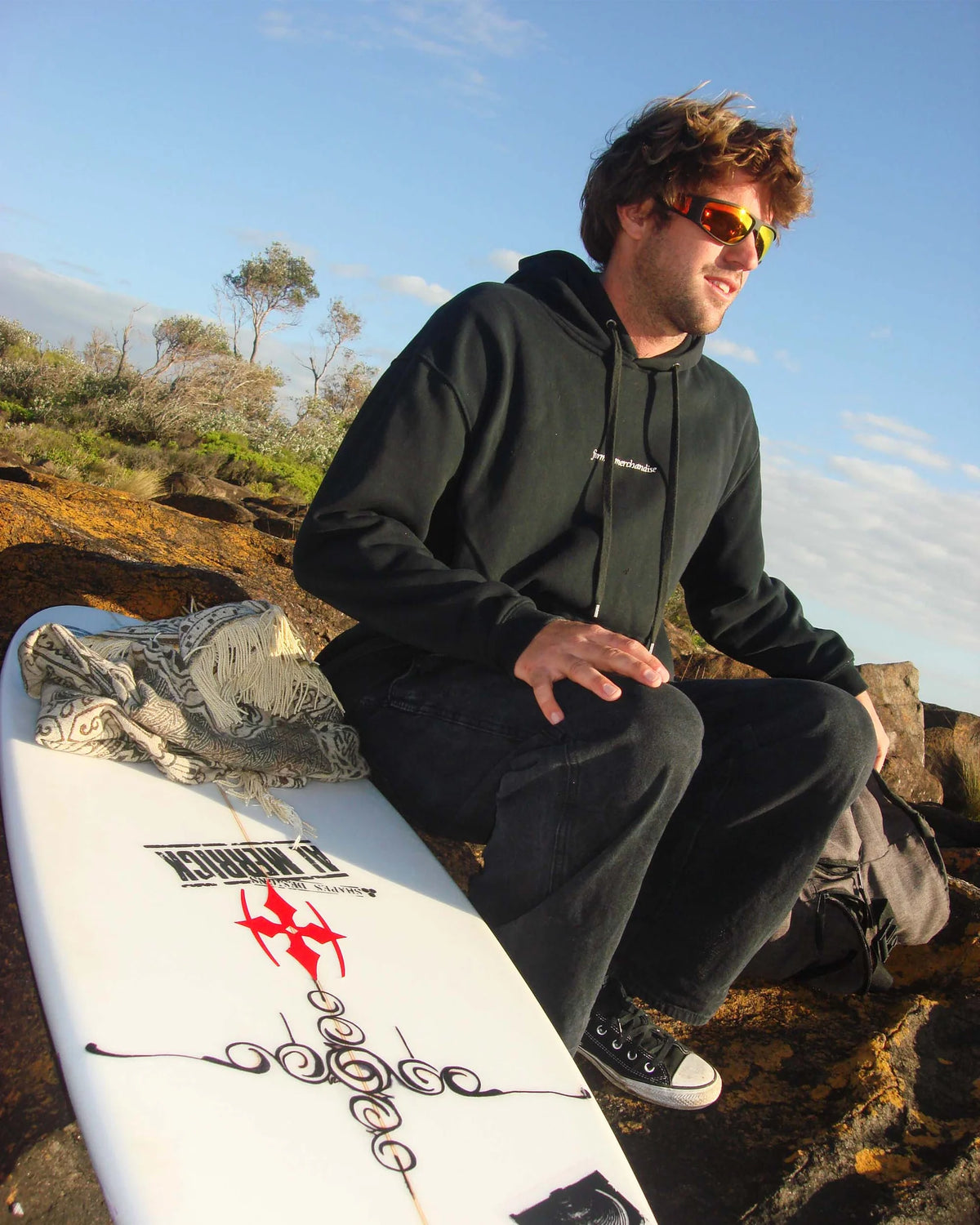 Model wearing Ritual Vision The Vacationer Sunglasses in Matte Black / Black Polarised seated with surfboard shed nine
