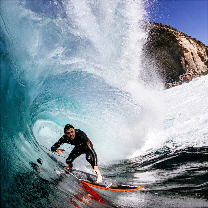 Surfer riding a wave in a black wetsuit with a colorful surfboard. shed nine