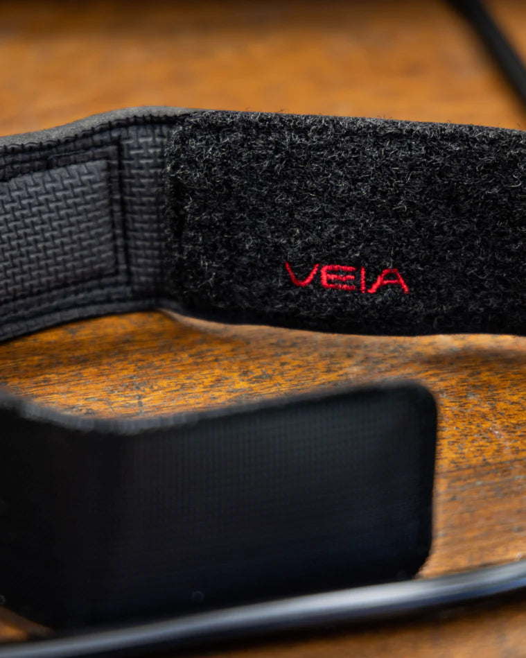 Black strap with 'VEIA' logo on a wooden surface shed nine