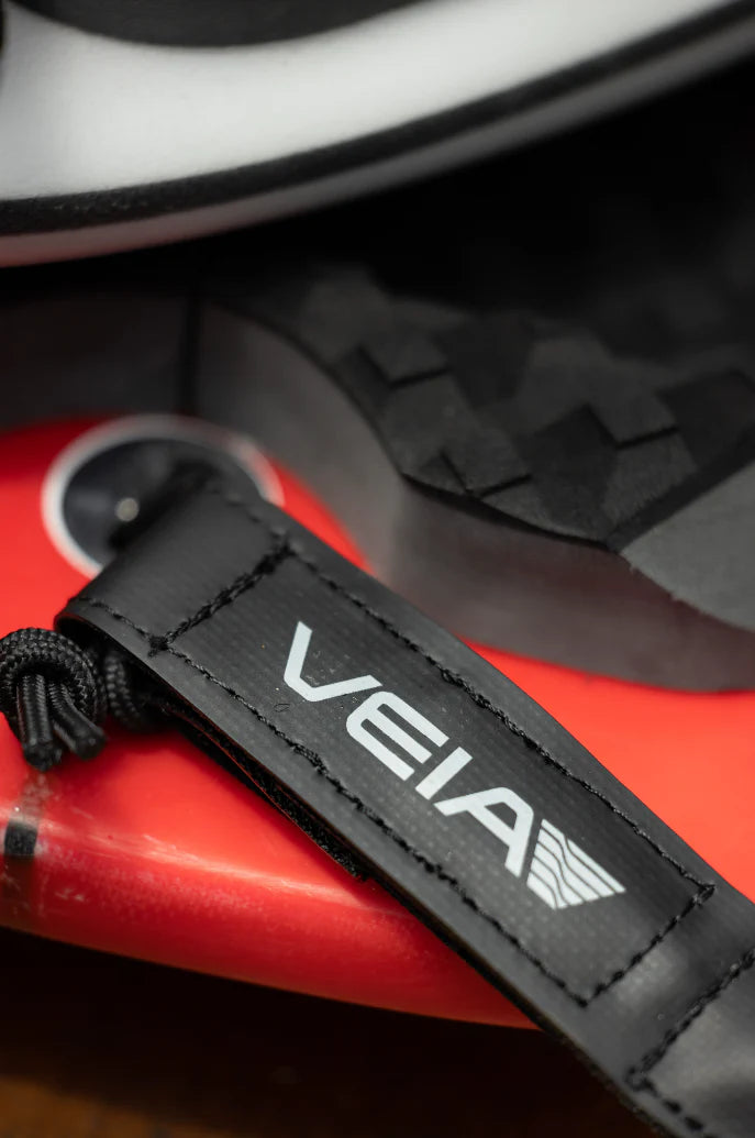 Close-up of a black strap with 'VEIA' logo on a red and gray background shed nine